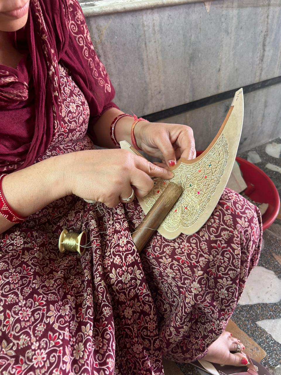 A woman from the Maniram household in Fazilka embroidering a jutti upper in tilla using the aari technique. The leather is held steady with a wooden danda (rod) placed between her legs, allowing her hands to move freely across the surface. (Picture Credits: Nandini Agarwal)
