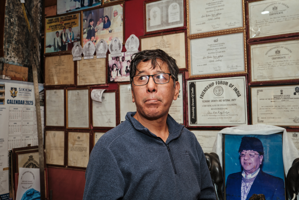Dhananjay Sakya next to the image of his father Babu Kazi Sakya and a wall displaying Babu Kazi Sakya's accolades. (Picture Credits: Abhishek Anil)