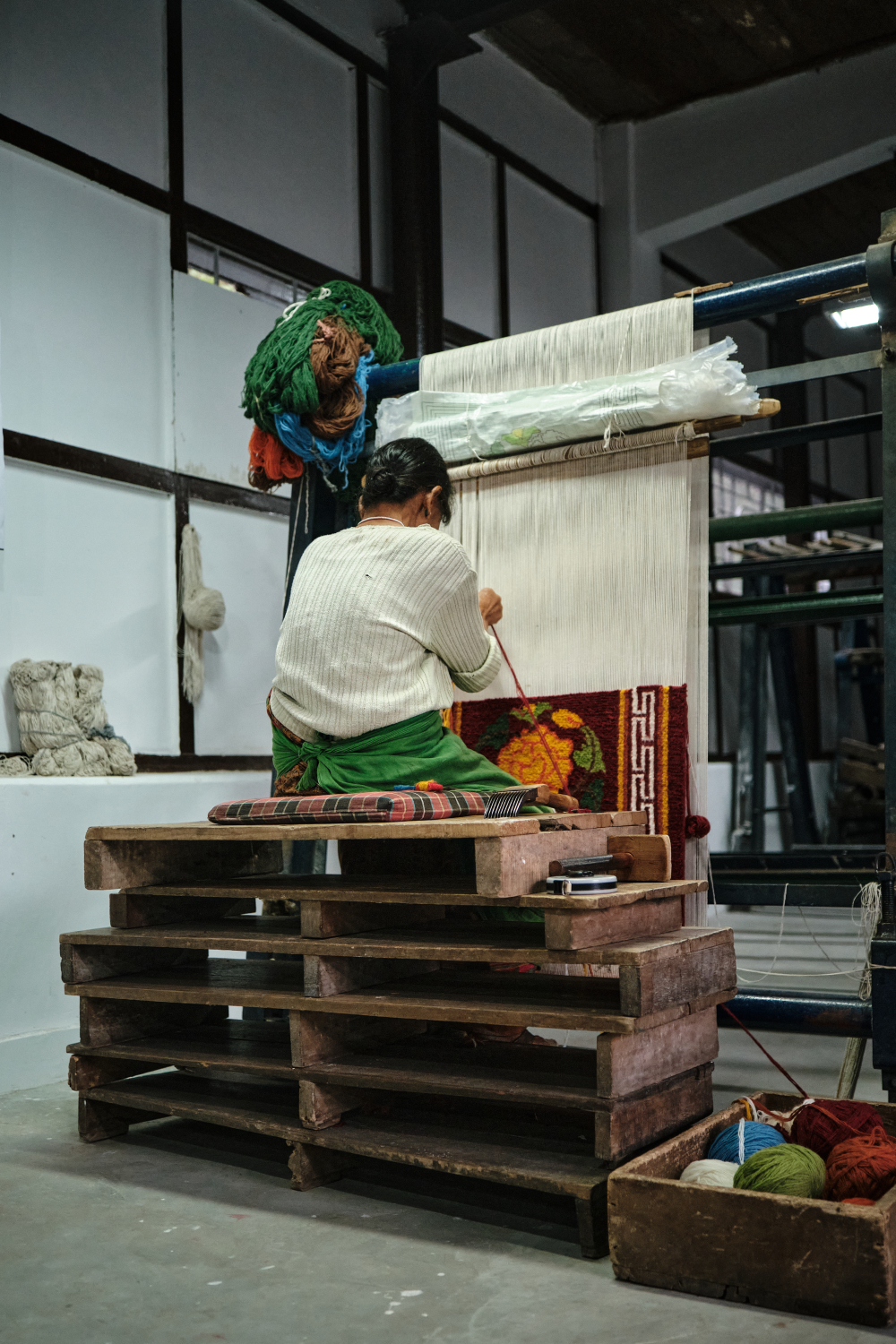 Lady sits on wooden steps to weave carpet. (Picture Credits: Abhishek Anil.)