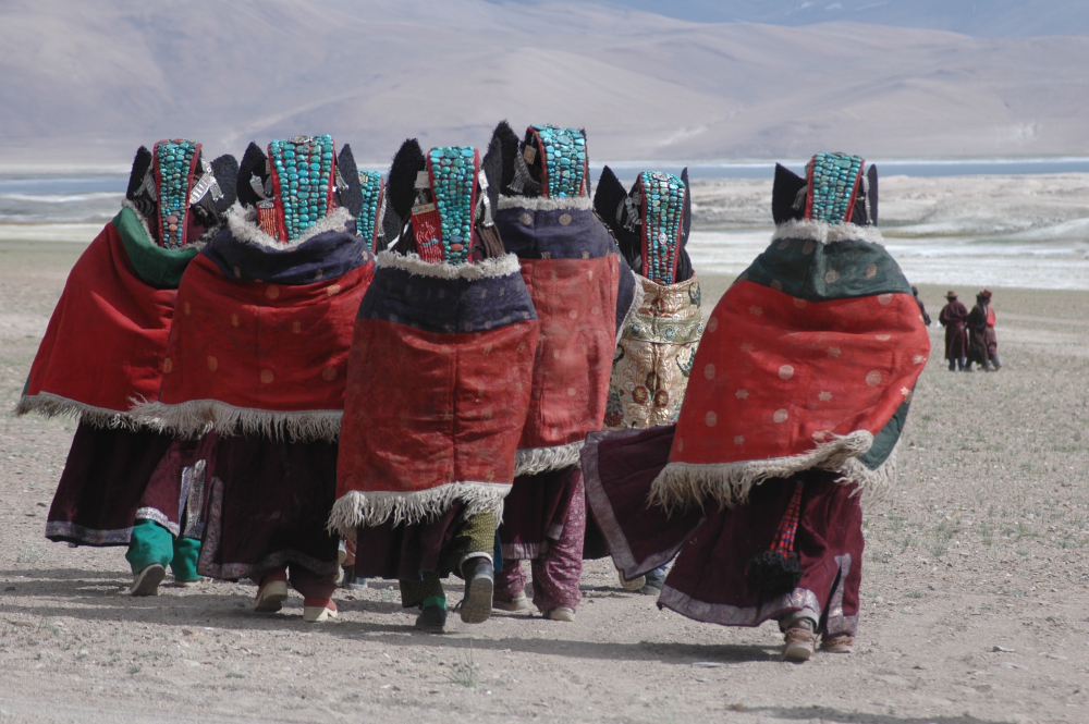 A group of women in Rupshu, Changthang, are all dressed up to attend a Horse Race near the Tso Khar lake. They are all wearing perags with four or five lines of turquoise. Also, visible, on either side of the head, are the silver chains (thenthak) holding the perag and earflaps in place. Two of the women, on the left, have the additional coral strip stitched on to the side of their perags. This is indicative of greater prosperity. A large yarn tassel (geblin) can be seen below the cape of the woman on the right. (Photographer: Monisha Ahmed, 2006)