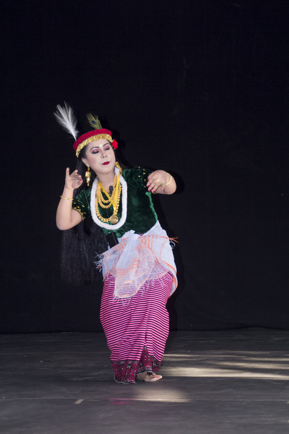 Fig. 1: A dancer performs the Khamba Thoibi dance, a thougal jagoi (dance in service of gods) performed during the Lai Haraoba (pleasing of the gods) festival, Manipur. Thoibi’s ensemble includes a phanek mayek naibi (striped phanek with embroidered borders), resom phurit (blouse made of dark green glossy fabric, embellished with sequins), white khwangyet (waistcloth) knotted at the centre, kajenglei (a red headdress with golden fringes and a peacock feather tucked on top) (Courtesy: Jawaharlal Nehru Manipur Dance Academy (JNMDA), Imphal).