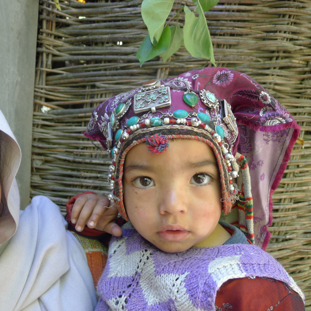 A young child in Turtuk, Nubra, wears an elaborate headdress of silver amulet boxes, turquoise, pearls and glass beads. These are stitched onto a purple cloth that covers her head and tapers down her back. As much for decoration, it is said to protect the child and ward away evil spirits. (Photographer: Tsering Wangchuk Fargo, 2014)