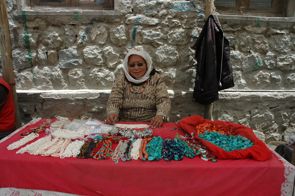 Fig. 12. A Tibetan trader sets up shop along the pathway in Leh market, selling coral, pearls, turquoise, and an assortment of silver pieces. Some of the stones are strung, while others are not. These are mainly flat turquoise pieces that Ladakhi women buy for their perags. She is wearing a necklace with one large central dzi (etched agate) and four smaller ones, strung together with coral stones. (Photographer: Monisha Ahmed, 2005)