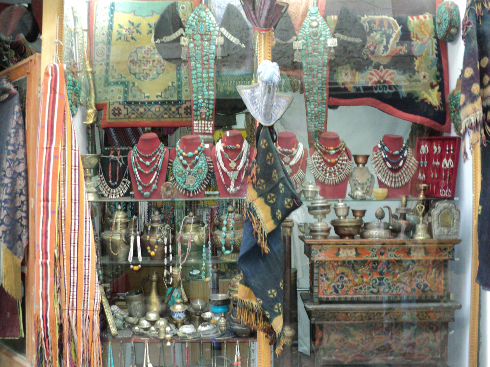 Fig. 13. The window of an antique shop in Leh shows old peraks and an assortment of old and new necklaces and earrings for sale. On the bottom shelf, centre, is a pair of conch-shell bracelets. Apart from an assortment of teapots, religious objects, textiles and low wooden tables. (Photographer: Zahera Bano,2010. Courtesy: LAMO Visual Archive)