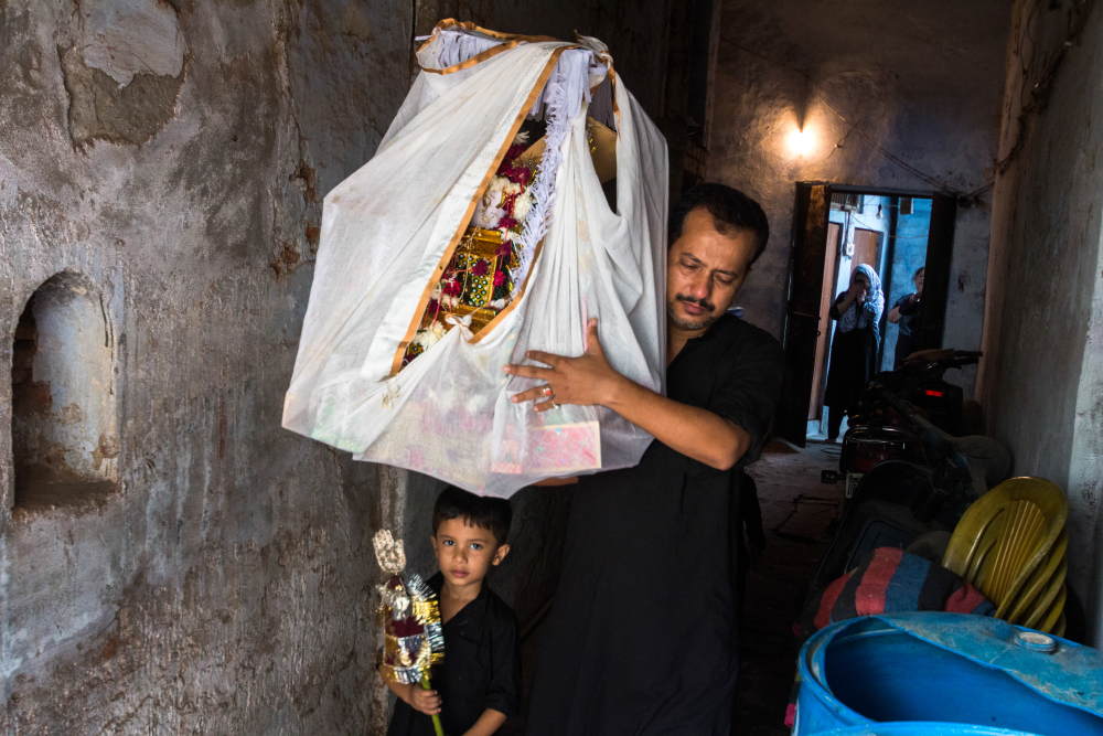 Fig. 7: A man with a child holding an alam (flag) takes a taziya for burial. The end journey of a taziya is usually on the tenth day of Muharram when it is draped in cloth with flowers that adorn it in an azakhana