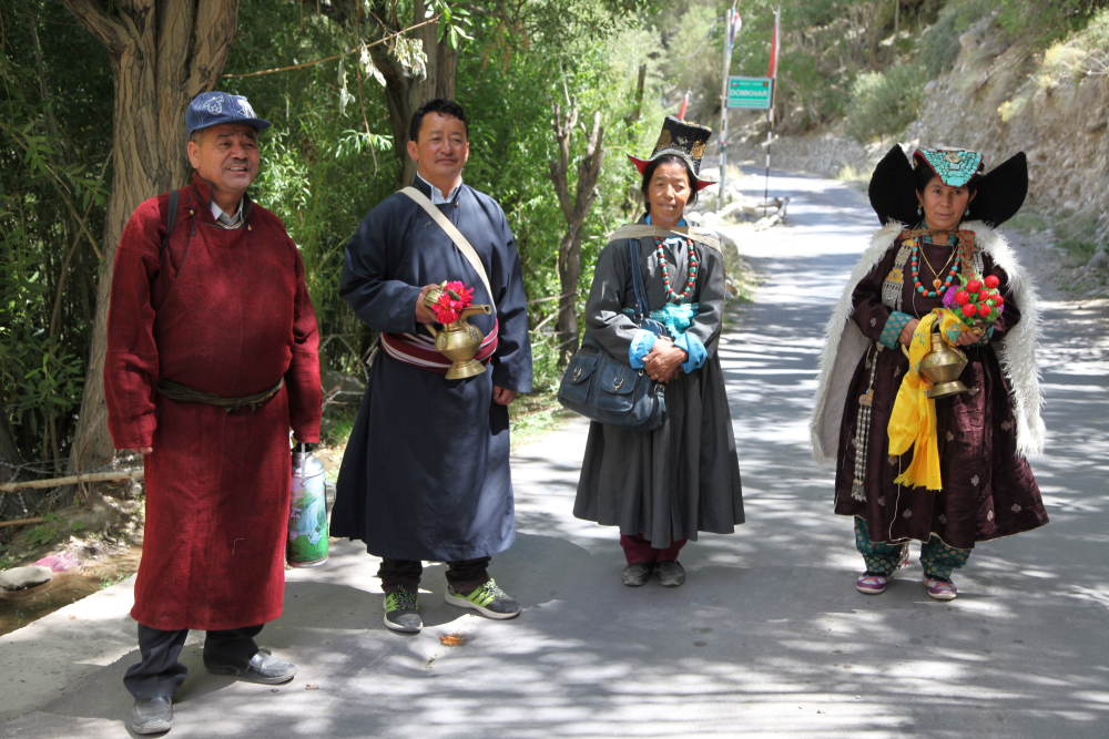 A group of people, dressed in their best, on their way to attend a ceremony at the monastery in Dumkhar village. The two men are dressed in the male robe (gos), while the one on the left wears one made from locally woven woollen fabric (snambu), the one on the right wears one stitched from imported polyester. The women are dressed in sulma, the one on the left wears one made from polyester with a machine-embroidered velvet hat (tibi).  The woman on the right wears a silk-brocade robe with a turquoise-studded headdress (perag). Over her shoulders she wears a cape (sbog) made from silk-brocade, lined with imitation goatskin. (Photographer: Tsering Wangchuk Fargo, 2015)