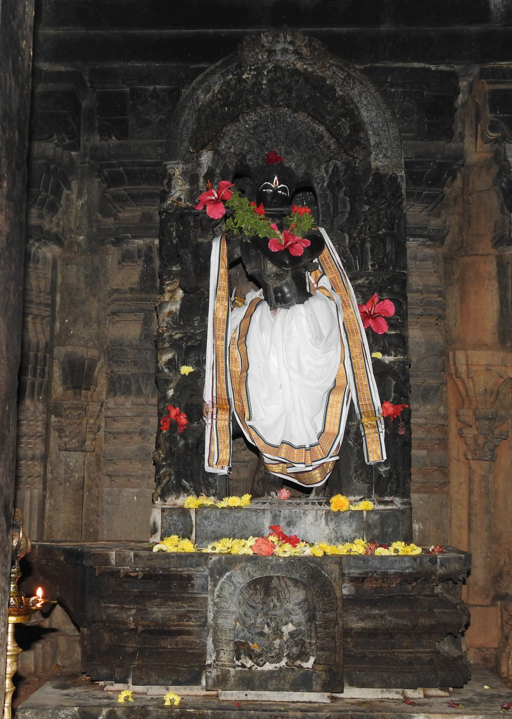 Fig. 3: The image of a standing Venugopala from the right garbhagriha. He is standing in cross-legged posture and is shown in the process of playing flute. Attendants, cowherds, and cows are carved on the parikara (an arch behind an icon depicting varied imagery, mostly related to the icon) of the image and Garuda is seen in anjalimudra on the pedestal.