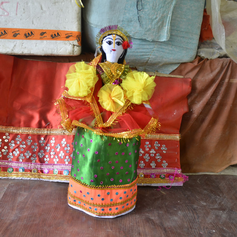 A laidhibi wearing a potloi, a green cylindrical skirt-like wrap. The red net worn around the waist is call boswan. Laces, trimmings, beads and artificial flowers are used to decorate the laidhibi (Courtesy: Akoijam Sunita)